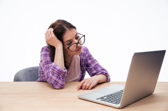 Tired female student in glasses sitting at the table with laptop over white background